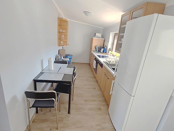 Wohnen auf Zeit – Küche – Schmale Wohnküche mit Einbauschränken, Esstisch, Kühlschrank und hellem Holzfußboden