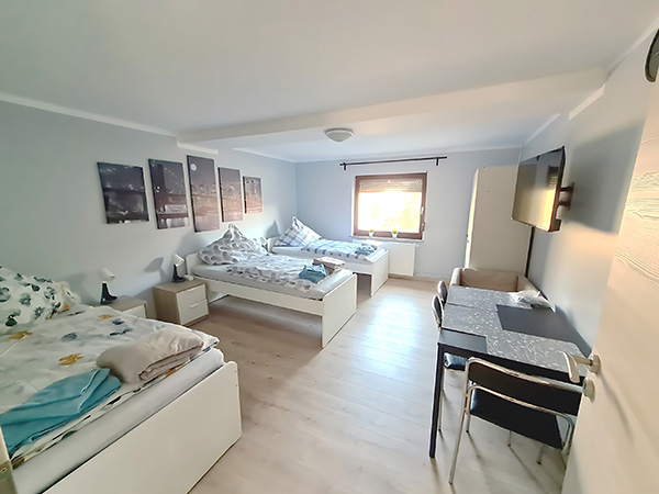 Wohnen auf Zeit – Schlafzimmer – Großes Mehrbettzimmer mit drei Einzelbetten, TV, Schreibtisch und hellem Fenster