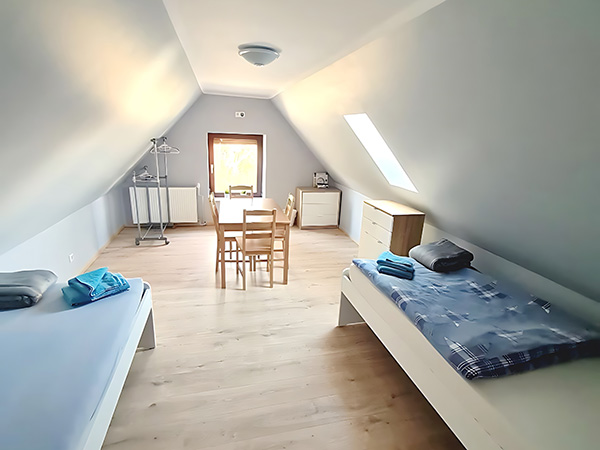 Wohnen auf Zeit – Schlafzimmer – Dachgeschosszimmer mit zwei Einzelbetten, Esstisch, Dachfenster und hellem Holzfußboden
